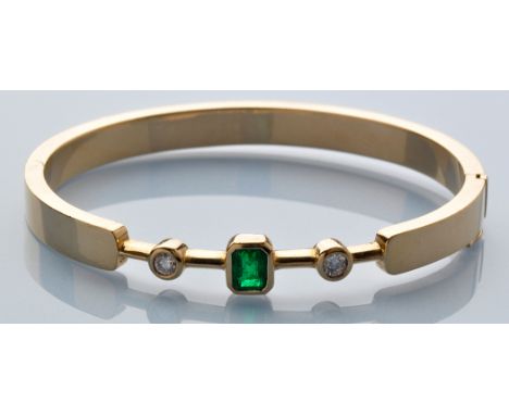 An emerald, diamond and yellow metal bangle, the rectangular facet cut emerald measuring approximately 5.8 x 4.6mm, within co