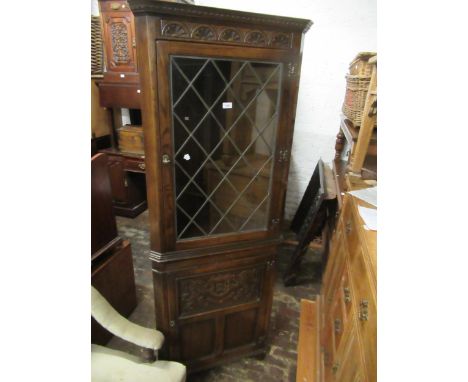 Reproduction oak standing corner cabinet with a leaded glass door above a carved panel door, on bracket feet, 73ins x 27ins 