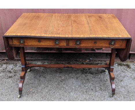 A Regency mahogany sofa table, having a crossbanded rectangular top and two fall flaps, two frieze drawers with lion ring mas