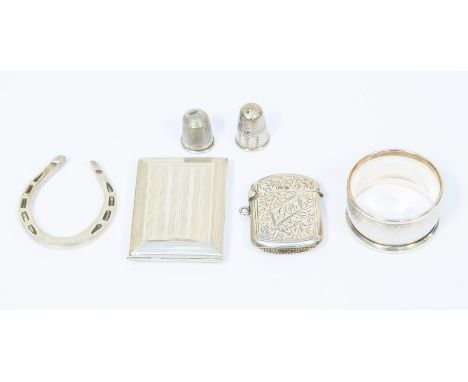 A silver match book holder, silver lucky horseshoe, napkin ring, two thimbles one is silver and a silver vesta case.