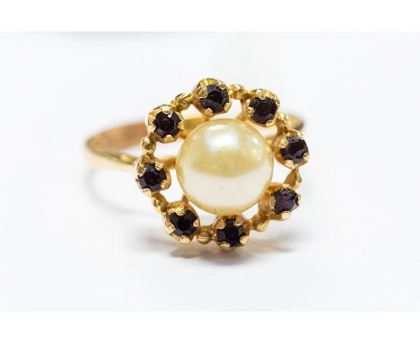 An 18ct. yellow gold, pearl and garnet ring, set central pearl surrounded border of eight claw set round cut garnets, shank i