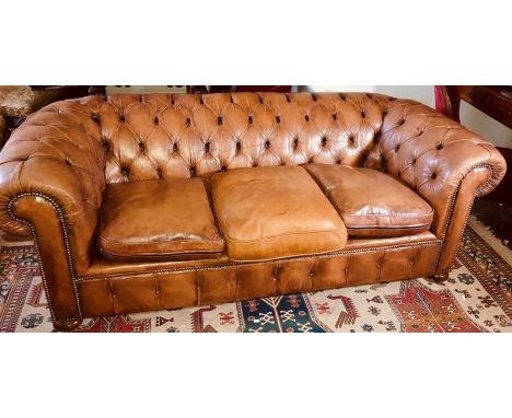 A Victorian revival tan leather three seater Chesterfield sofa, scrolling button back and arms, brass studded decoration, rai