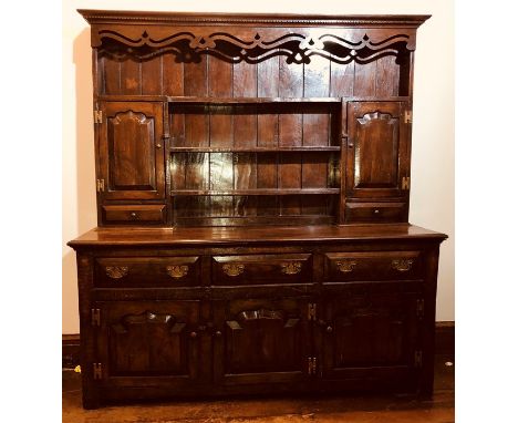 A George III oak dresser, circa 1760, moulded dental pediment above carved foliage top on three tier plate rack shelves, flan