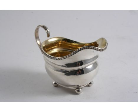 A GEORGE III MILK JUG on bun feet with a flying scroll handle, gadrooned border & gilt interior, by R. Emes & E. Barnard, Lon