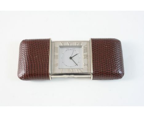A BRASS TRAVELLING CLOCK BY TIFFANY & CO. with Roman numerals, quartz movement, brown leather slide action case,9cm. dia. whe