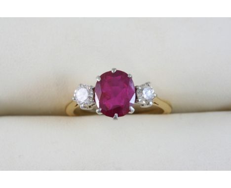 A RUBY AND DIAMOND THREE STONE RING the central oval-shaped ruby weighs approximately 2.30 carats, and is set with two circul