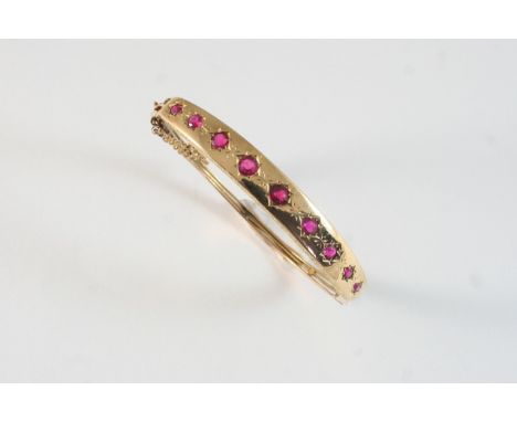 A GOLD HALF HINGED BANGLE set with graduated circular-cut synthetic rubies in 15ct. gold. With box.