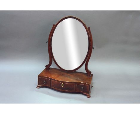 A GEORGE III MAHOGANY TOILET MIRROR the serpentine plinth with boxwood stringing, fitted with three short drawers, on ogee br