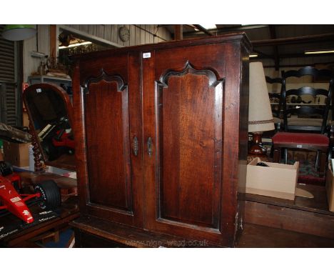 A Georgian Oak Wall Cupboard having moulded edge plank top, pair of opposing single raised and fielded, shaped top panel door