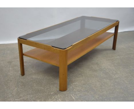 MANNER OF G PLAN, a teak coffee table, with smoked glass top, on a teak base with shelf, 35cm high x 115cm wide x 47.5cm deep