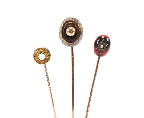 Three cased 19th century yellow metal stick pins. The stick pins including garnet glass cabochon mounted with a pearl set sta