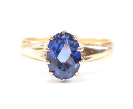 A gold and synthetic sapphire solitaire ring. The ring set with an oval cut synthetic sapphire to stylized shoulders and plai