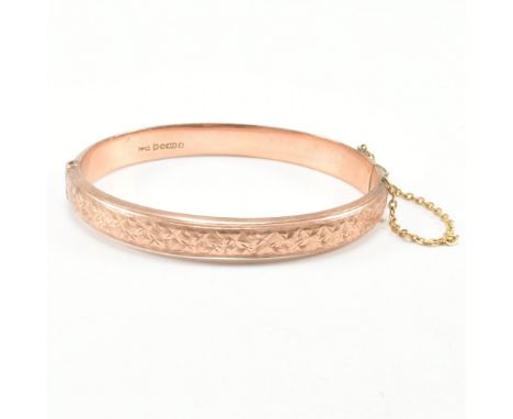 An Edwardian hallmarked 9ct gold bangle. The antique hinged bangle having chased foliate decoration with safety chain to conc