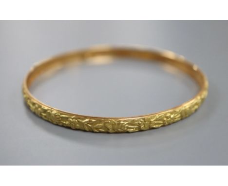A yellow metal (tests as 18ct) bangle cast with continuous band of flowers, 9g, interior 64mm.