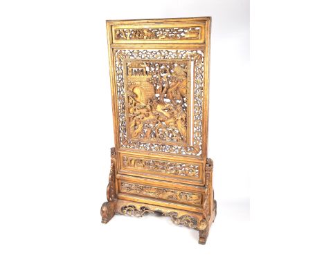 A Chinese giltwood reticulated table screen, late Qing DynastyThe scroll tab sides, supporting a central pierced panel, depic