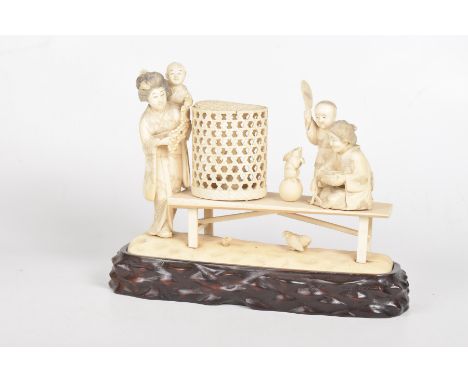 A Japanese ivory carving, Meiji periodModelled and carved a woman and children seated on a bench, feeding chickens and rabbit