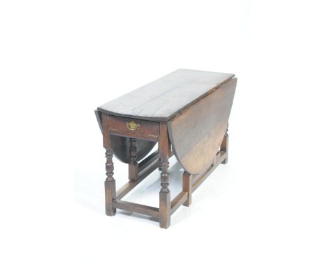An 18th Century oval oak dropleaf dining tableThe oval top above a single frieze drawer with brass drop handle, raised on rin