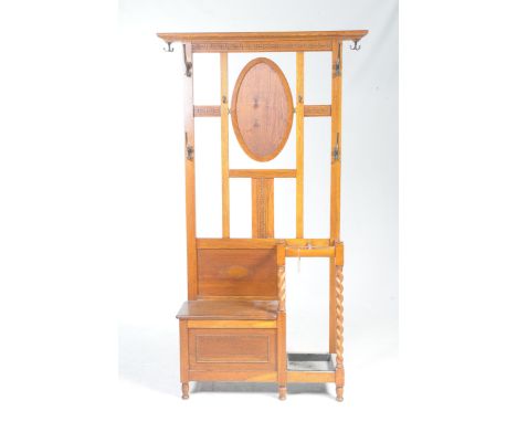 A 1920's golden oak hall standHaving a moulded top rail above a Greek key pattern frieze and a central oval swing panel, the 