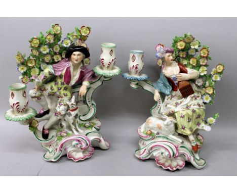 A PAIR OF CHELSEA DERBY CANDLESTICK GROUPS, a man and woman with dog, standing before a bocage.Gold Anchor mark.  10ins high.