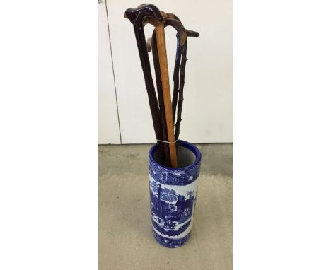 A blue & white ceramic stick stand complete with a quantity of walking sticks.