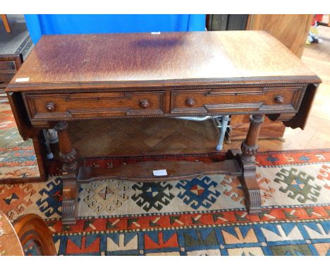 An oak drop flap sofa table, with moulded edge top, frieze drawers on twin turned pedestal supports united by platform base o