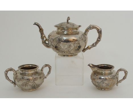 A CHINESE SILVER THREE PIECE TEA SERVICE decorated with birds amongst blossoming branches, with faux bamboo handles, the teap