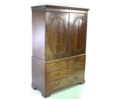 A George III mahogany linen press enclosed by oval panel doors, the base of two short over two long drawers on bracket feet, 