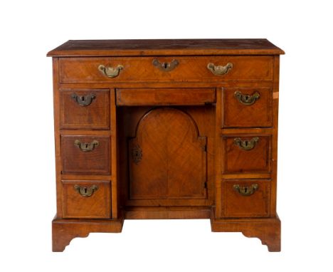 A George I style walnut veneer kneehole writing desk, circa 1720, with cross and featherbanded top above a frieze drawer and 