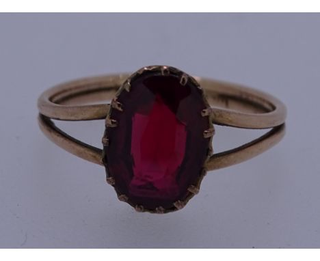 A BELIEVED GOLD (UNMARKED) RING with an oval ruby on split shoulders, 2.5grms, size N/O