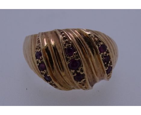 A 9CT GOLD DRESS RING with three rows of tiny rubies in a wavy style setting, 5grms, size O