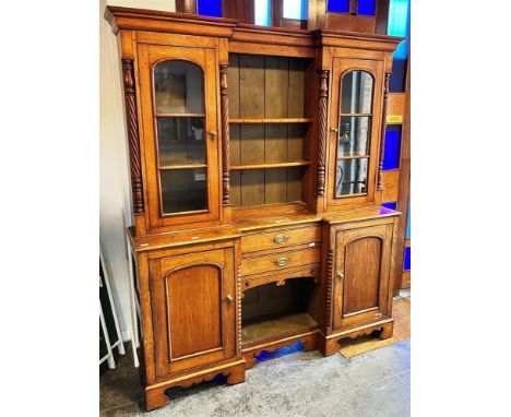 A VICTORIAN OAK INVERTED BREAKFRONT DRESSER  the upper section with shelves flanked by glazed cabinets with spiral pilasters,