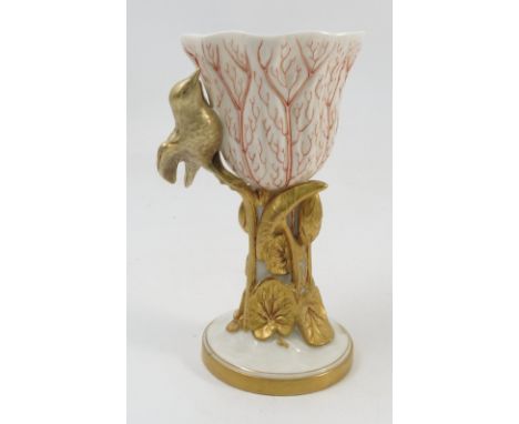 A Royal Worcester gilded ivory vase, the moulded flower bowl with painted red veins, having a moulded gilt bird to the side, 