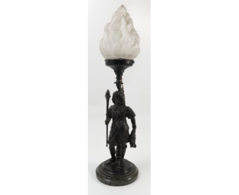 A spelter lamp base, formed as a cavalier soldier holding a flaming torch, with glass flame shade, raised on a circular stepp