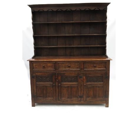 An oak dresser, with close boarded Delft rack over three drawers to the base, and two part carved cupboard doors below, by Th