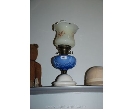 A ceramic Oil Lamp with white base, ornate blue reservoir and floral glass shade.