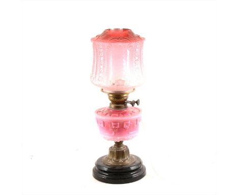 An oil lamp, adapted as a table lamp, brass column, strawberry tinted reservoir, and with a tinted shade, overall 57cm.