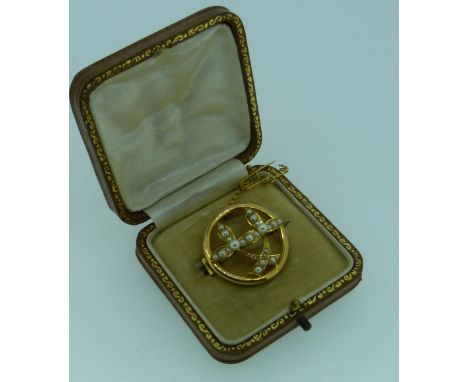 An open circular Brooch, in unmarked yellow metal, the centre set with two seed pearl set trefoils, safety chain attached, wi