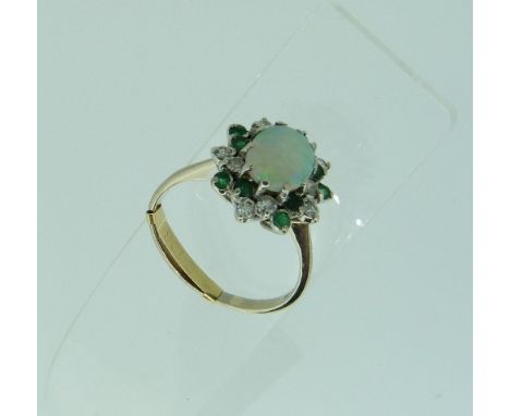 An oval cluster Ring, the central oval opal surrounded by a border of small circular cut diamonds and emeralds, all mounted i