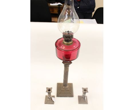 An early 20th century silver plated oil lamp, with a cranberry glass tank, raised on a Classical style column with a Corinthi