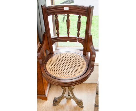 A late Victorian mahogany desk chair, bar and spindle back, circular drop in caned seat, cast iron base with tripod lion mask