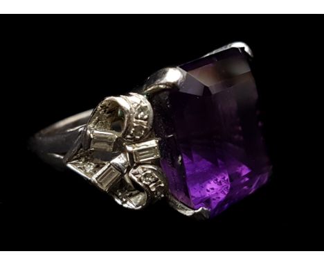 An amethyst and diamond dress ring, the central stone flanked by ribbon bows of brilliant and baguette cut diamonds, in white