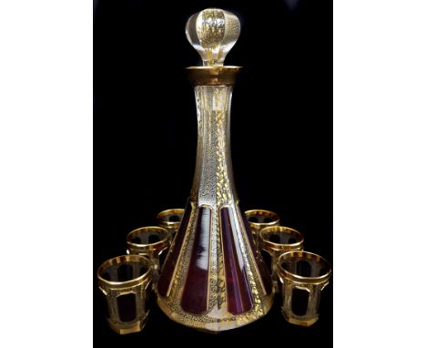 A Bohemian cased glass liqueur set, ruby cut through to colourless glass with 'jewel' panels on a vermiculated and vine gilde