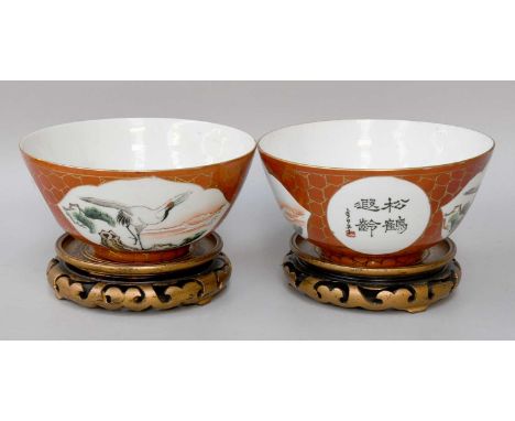 A Pair of Chinese Porcelain Bowls, 20th century, coral ground and with panels of cranes and calligraphy, 17cm diameter on woo