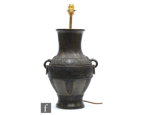 A Chinese cast metal archaic vase, Hu, rising from a high footring and applied with two loop and ring handles, cast with taot
