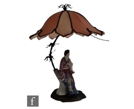 An early 20th Century Japanese ceramic lamp base, modelled as a bijin resting on a tree and reading a book, dressed in tradit