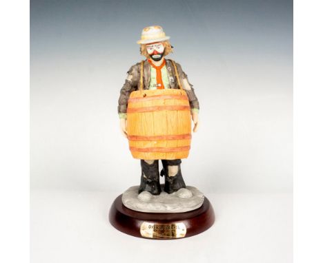 Hand painted porcelain figure of a clown wearing a barrel. Sits on a wooden round base with gold-tone titled plaque. Emmett K