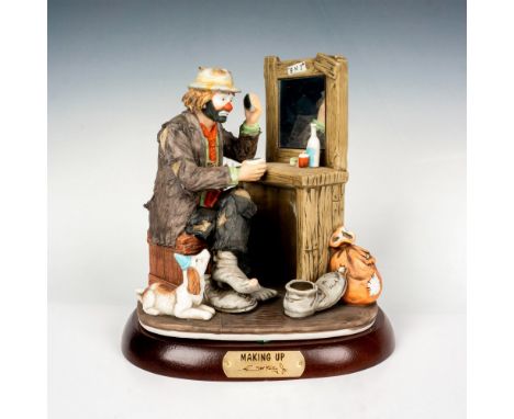 Hand painted porcelain figure of a clown putting on make up. Sits on a wooden base with gold-tone titled plaque. Emmett Kelly