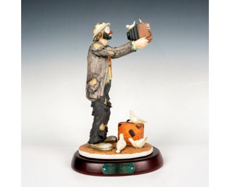 Bisque porcelain figural of the character Weary Willie standing holding a camera to take a picture of himself. Birds are seen