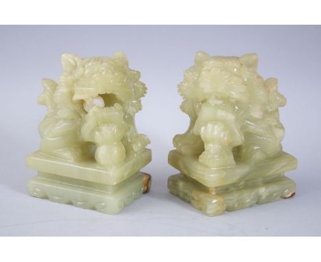 A PAIR OF 20TH CENTURY CHINESE JADE / JADELIKE HARDSTONE LION DOGS,  both sat upon carved pedestal bases with their paws upon