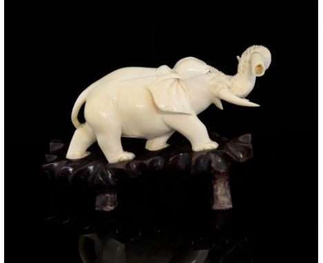 Japanese carved ivory elephant in a walking pose, with a tusk in it's trunk, on hardwood base, elephant 13cm long,